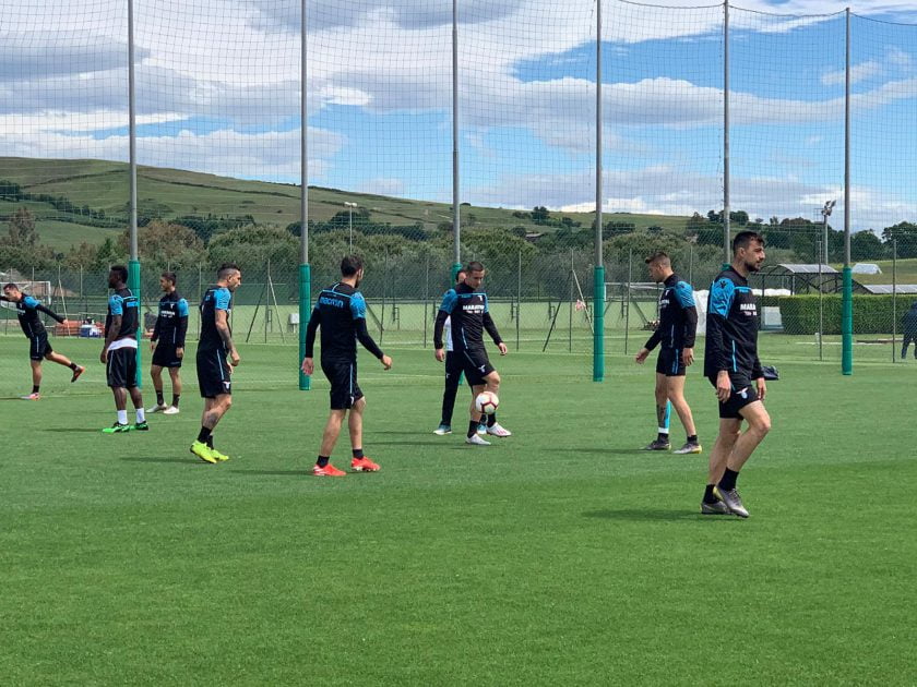 Una foto del centro sportivo di Formello, con un gruppo di giocatori e lo staff che si confrontano in un cerchio, a simboleggiare l'incontro.