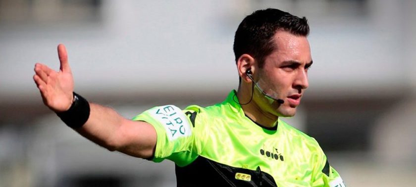 L'arbitro Colombo consulta il VAR durante Udinese-Lazio mentre i giocatori protestano.