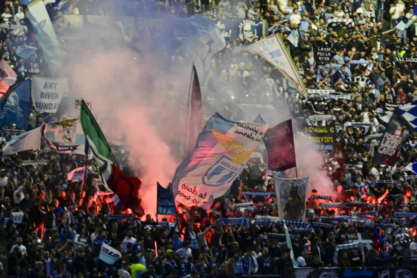 Una panoramica della Curva Nord dello Stadio Olimpico piena di tifosi della Lazio con bandiere e sciarpe.