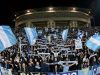✈️ Milan-Lazio, è Esodo: Oltre 2.000 Tifosi Biancocelesti Pronti a Invadere San Siro! Una curva gremita di tifosi della Lazio in trasferta allo stadio San Siro di Milano, che sventolano bandiere biancocelesti e sciarpe durante una partita notturna.